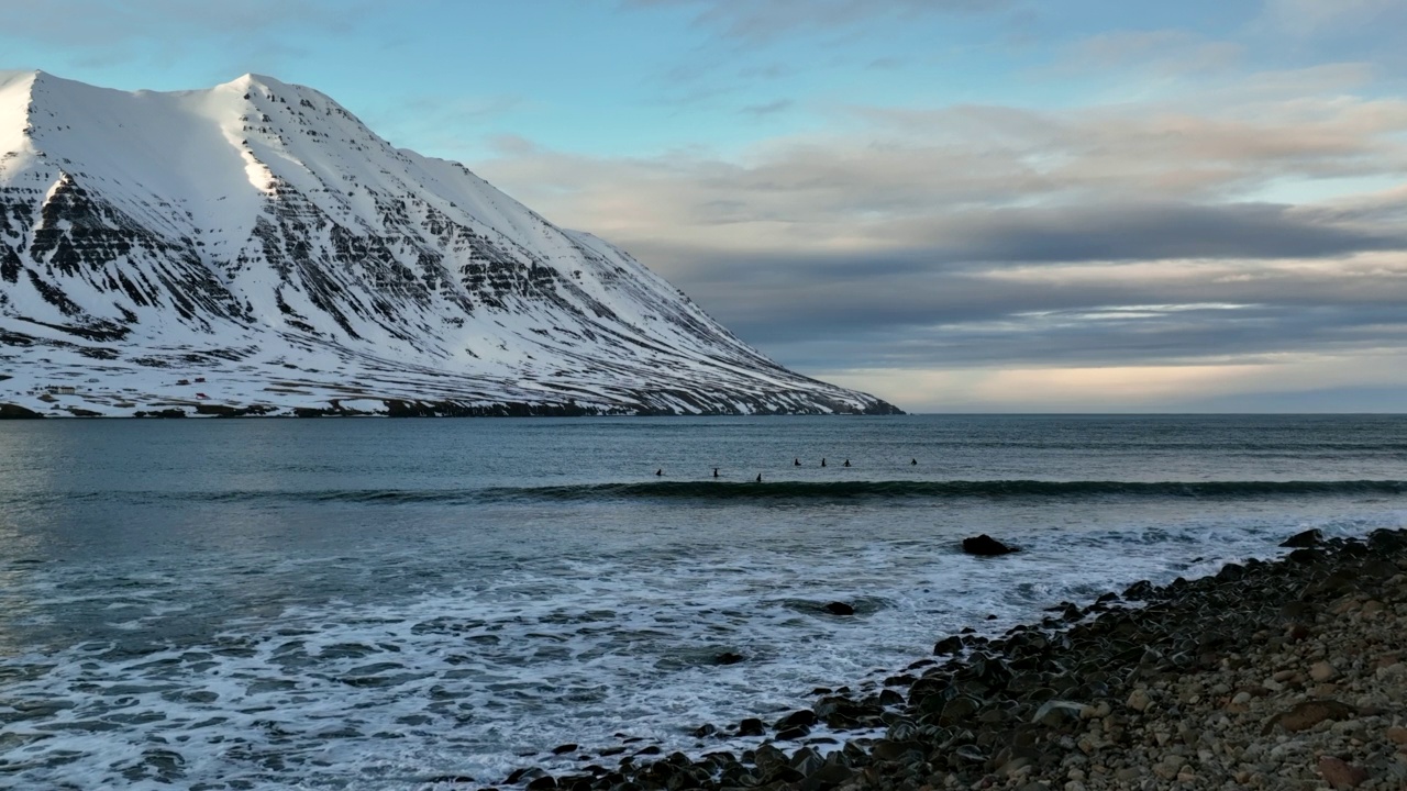 慢动作向前拍摄的人们在天空下的雪山度假时在波浪形的湖上冲浪-冰岛瓦特纳冰盖国家公园视频素材