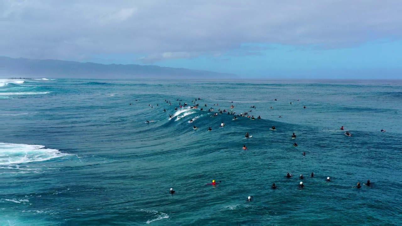 空中拍摄的男性冲浪者在多云天空下的海滩上冲浪的海浪-怀基基，夏威夷视频素材