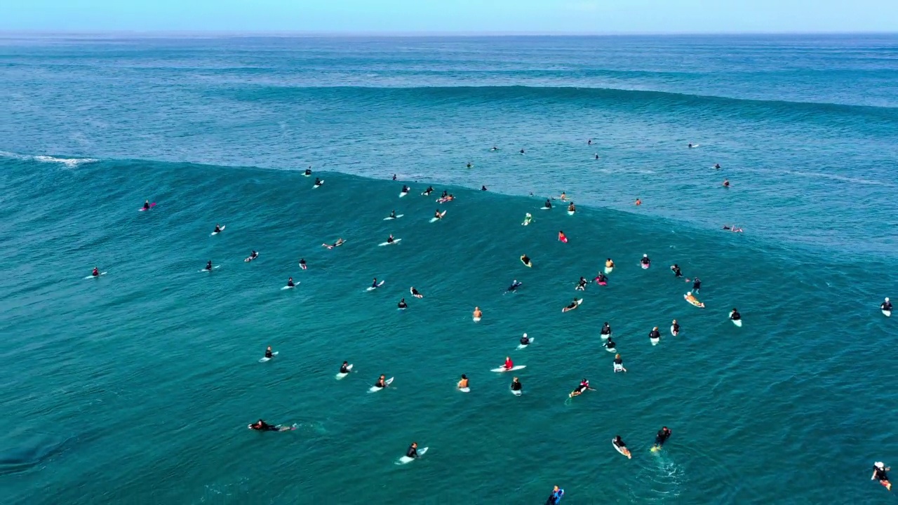 度假时人们拿着冲浪板在波涛汹涌的大海中游泳的航拍倒拍——夏威夷的威基基视频素材