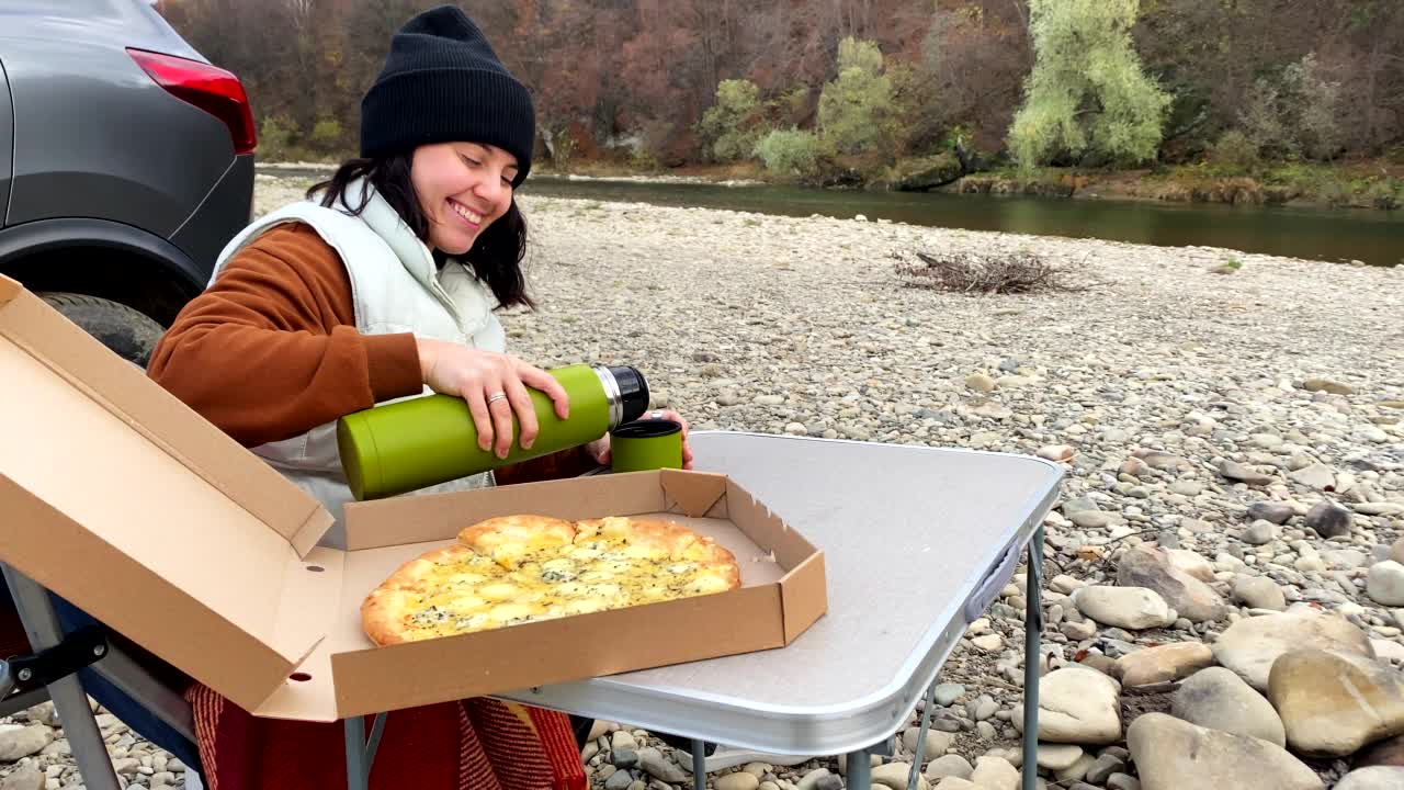 秋日，在秋山河滩野餐的女子一边倒茶，一边享受着温暖的天气视频素材