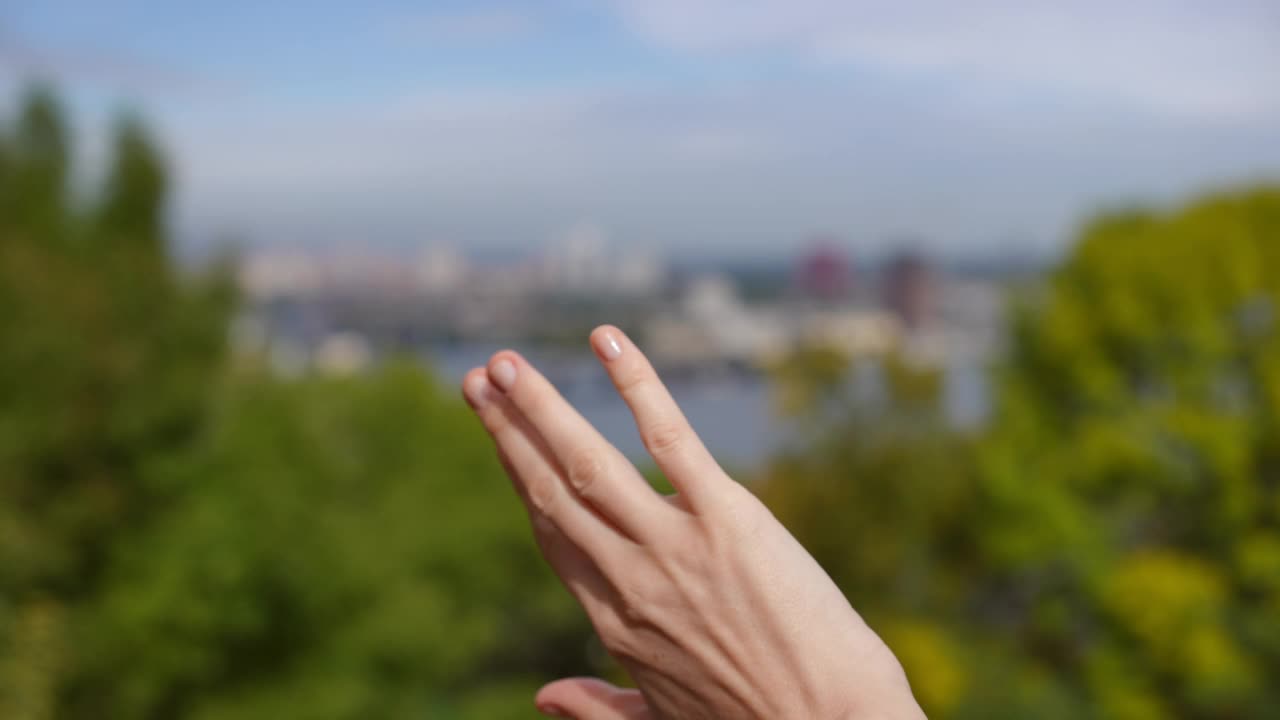 在户外模糊的城镇和河流背景下，女性的手在阳光下挥舞。无法辨认的白人苗条年轻女子在公园享受周末休闲。生活方式和宁静。视频素材