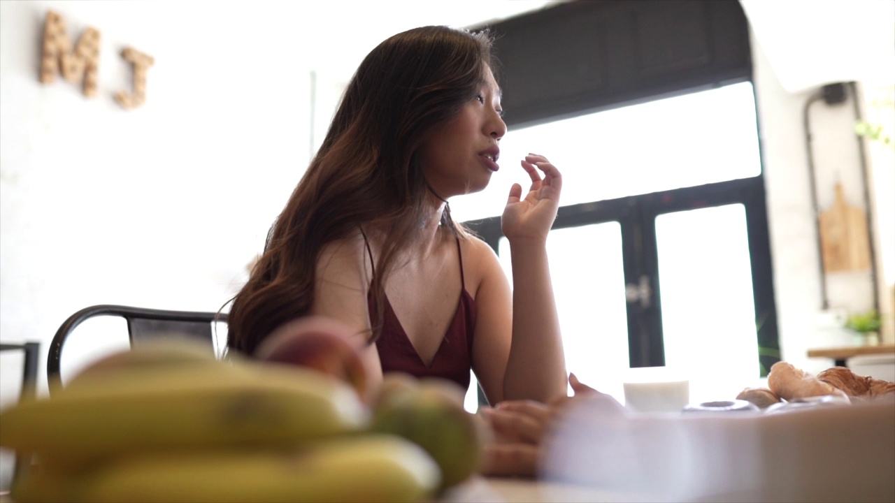 漂亮的亚洲女人在家里吃羊角面包早餐视频素材