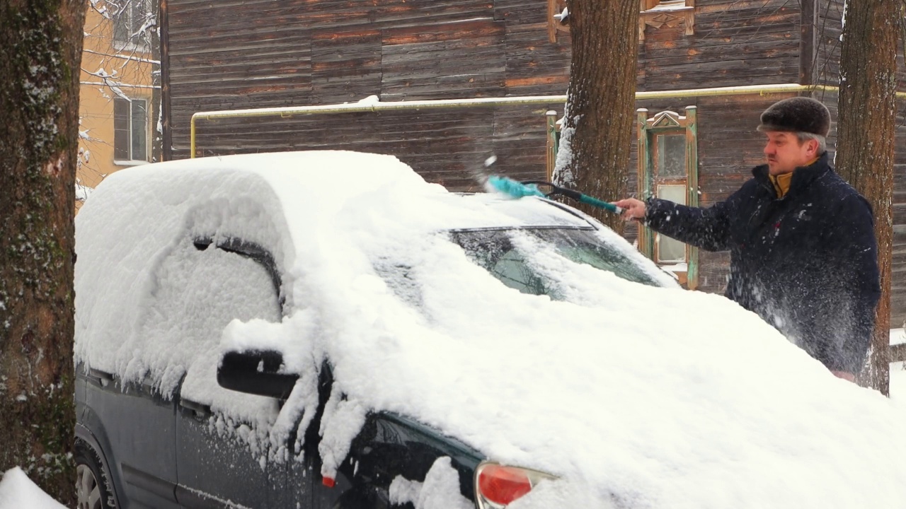 一个人用刷子清理汽车挡风玻璃上的雪，天正在下雪。视频素材