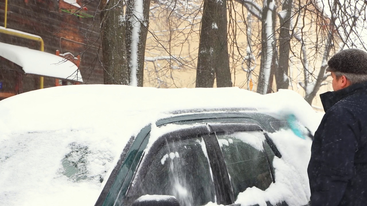 一个人用刷子清理车顶上的雪，天在下雪。视频素材