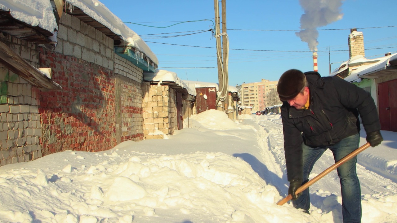 一名男子灵巧地用木铲清除通往车库的道路上的积雪。视频素材