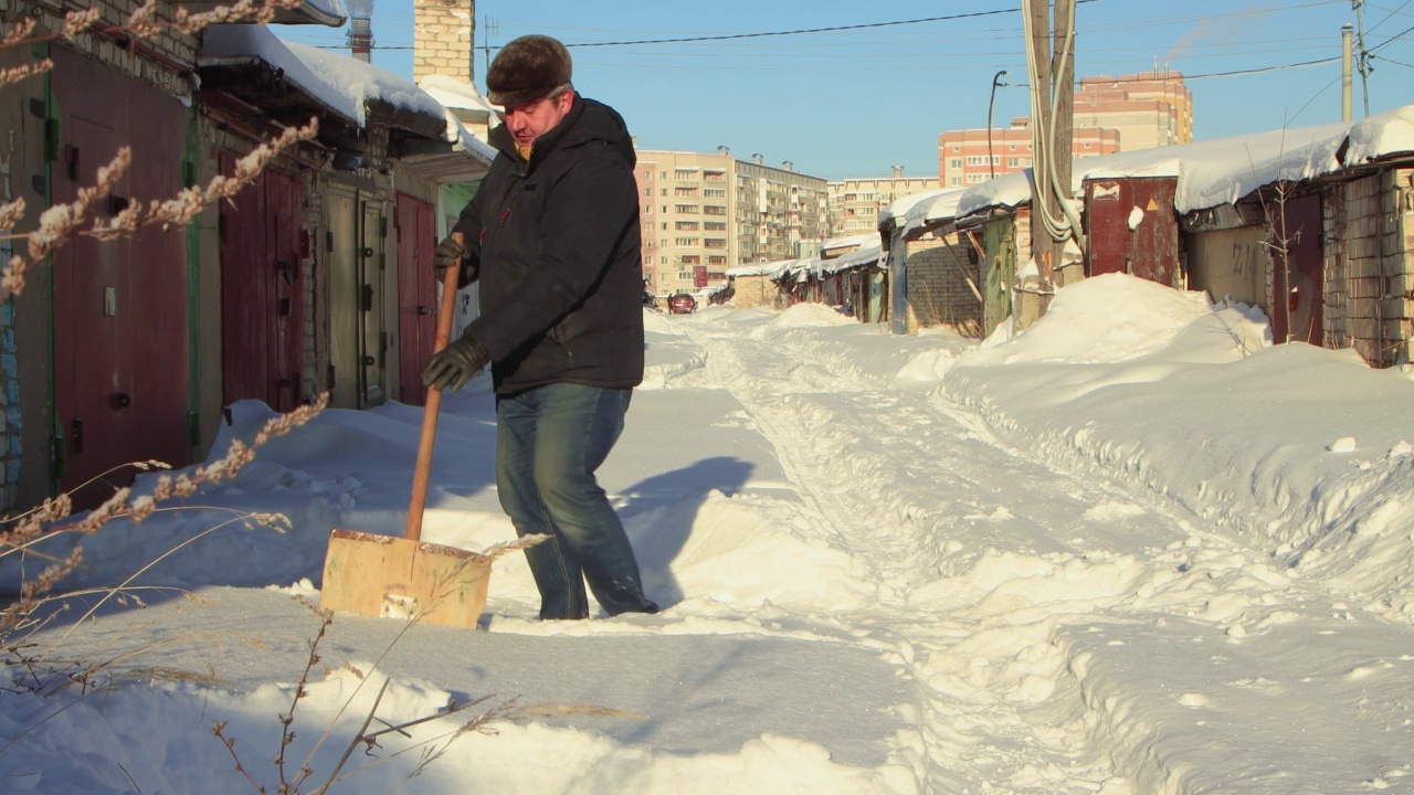 一名男子愉快地用木铲清理通往车库的积雪。视频素材