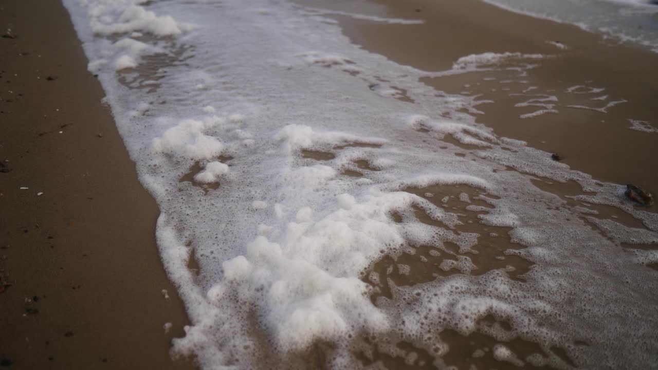 海浪泡沫被风吹到沙滩上的慢镜头。在狂风暴雨的日子里，浪花在海岸上飞溅。缓慢的运动。视频素材