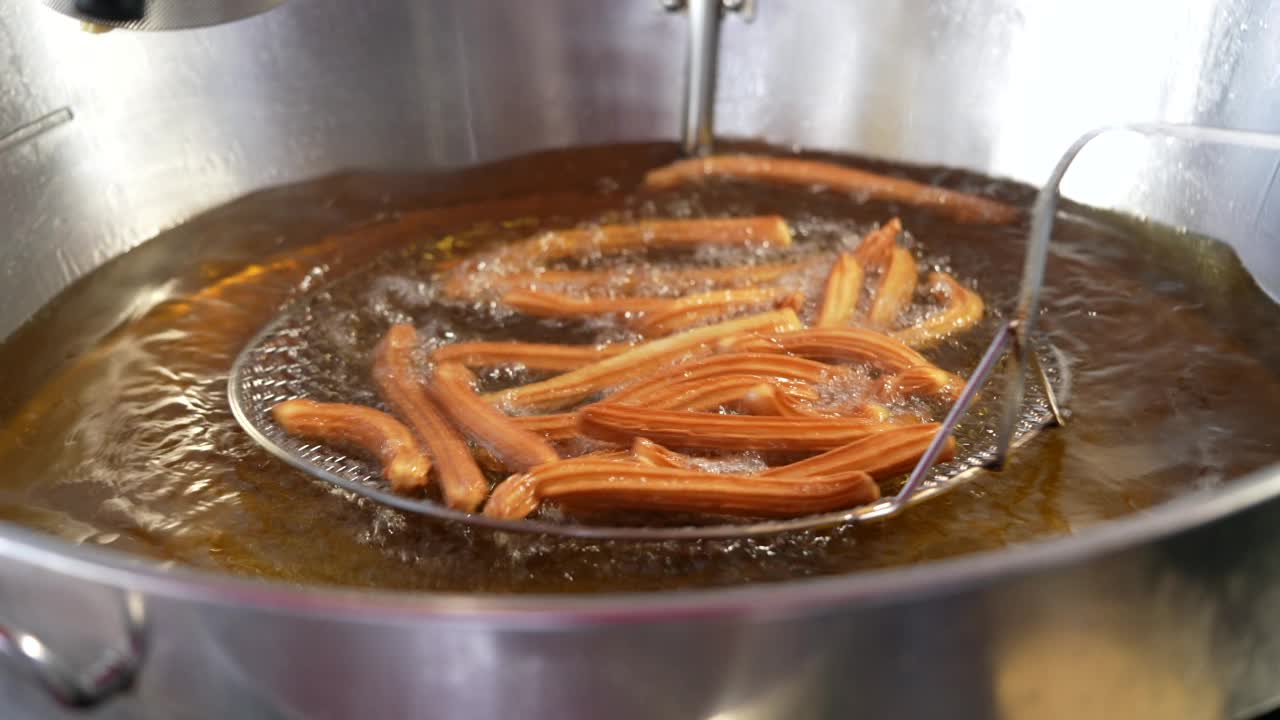 准备炸油条。街头小吃摊在油锅里准备油条。西班牙传统食品视频素材