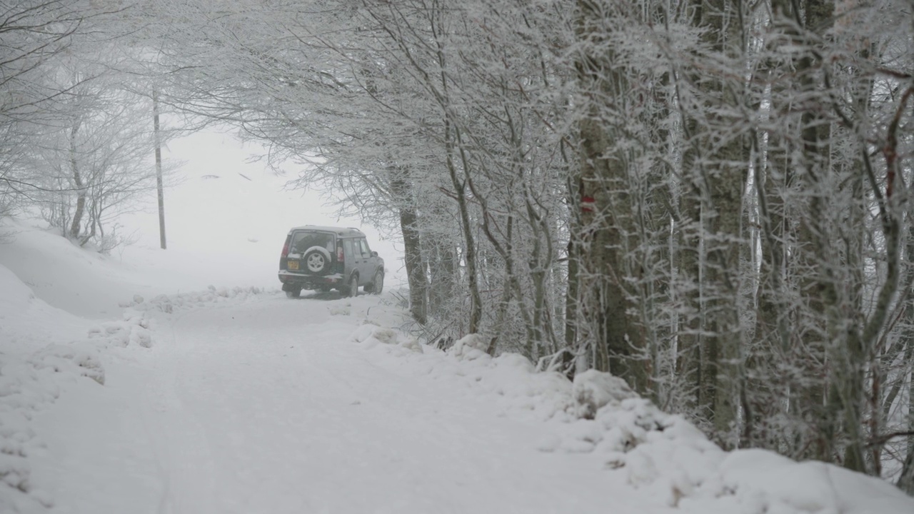 越野车探索者行驶在冬季积雪覆盖的道路上，穿过山林，慢镜头视频素材