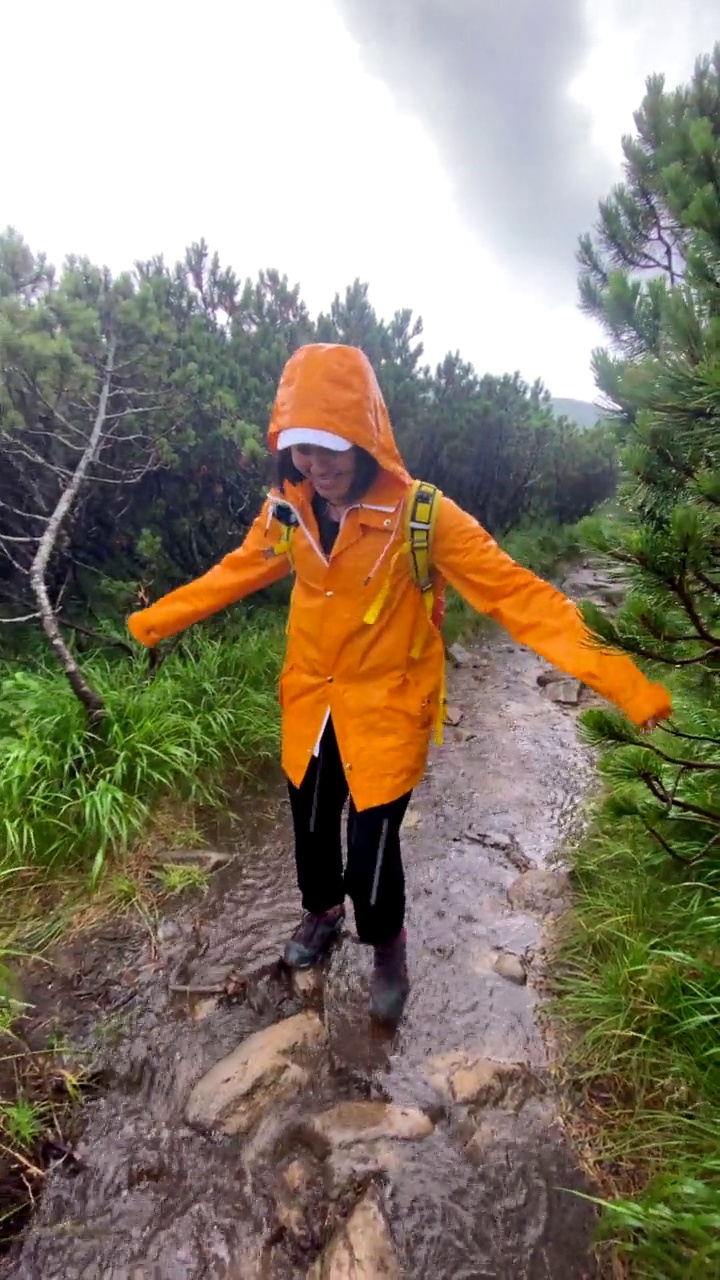 穿着黄色雨衣的女人在雨天沿着岩石小道走视频素材