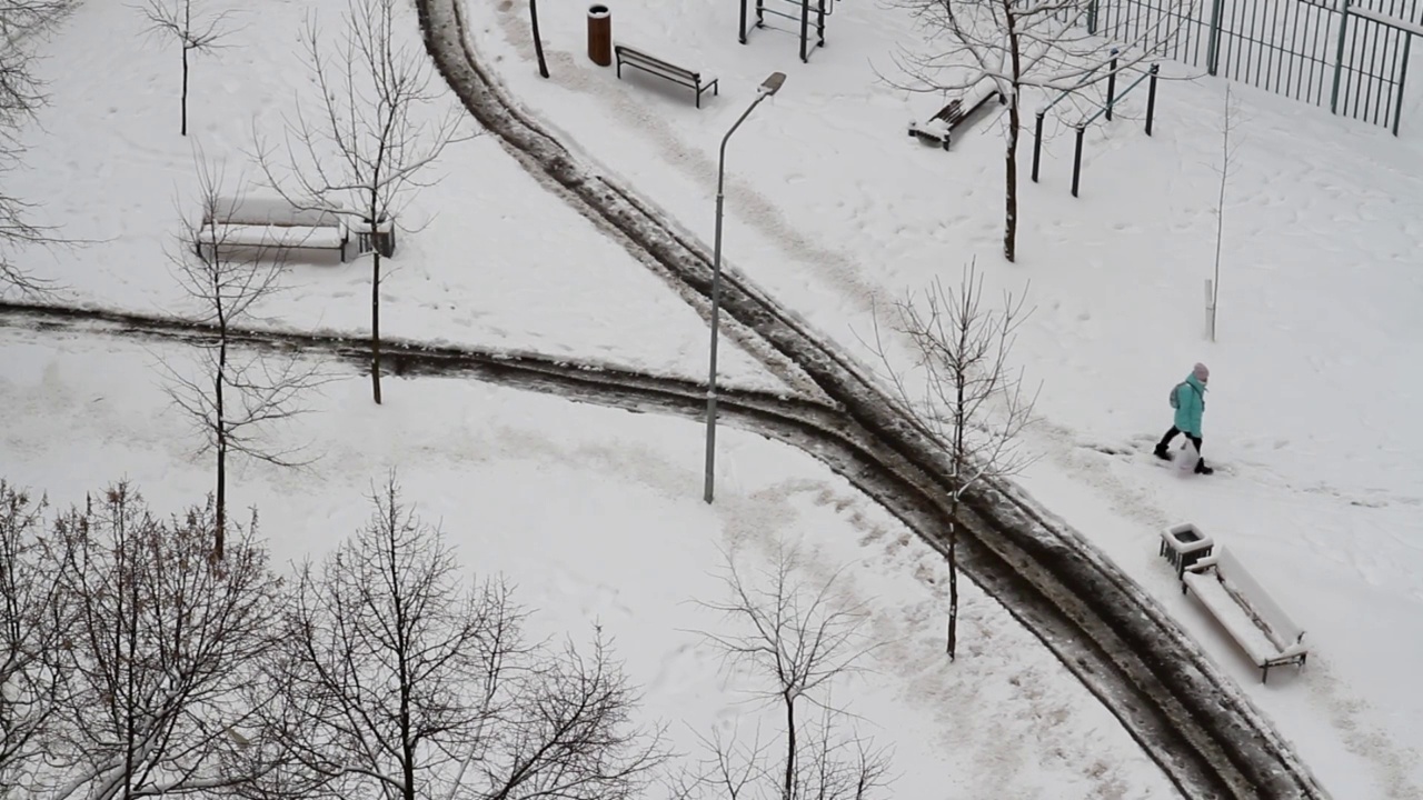 在城市的院子里，一个女学生走在一条被雪清理过的道路和一条被雪覆盖的道路上视频素材