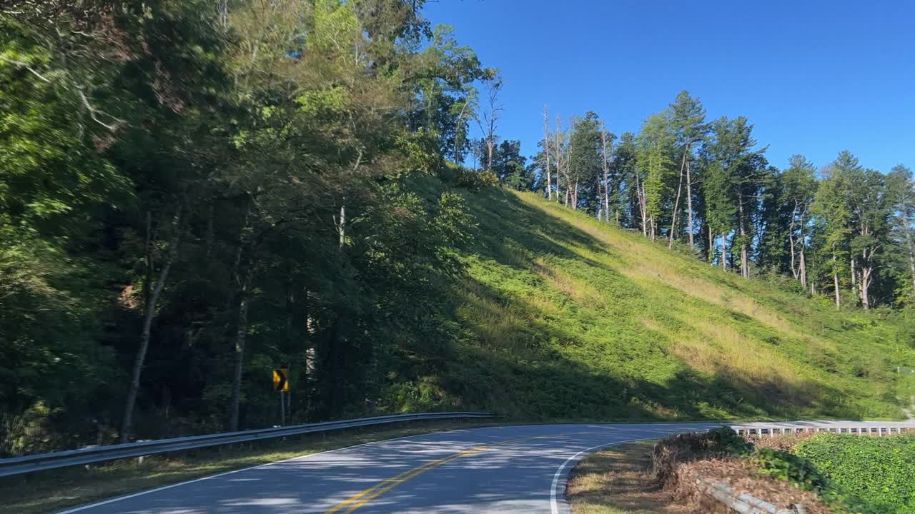 在一个阳光明媚的下午，沿着北卡罗莱纳州蓝岭山脉的一条绿树成荫的高速公路开车转弯视频素材