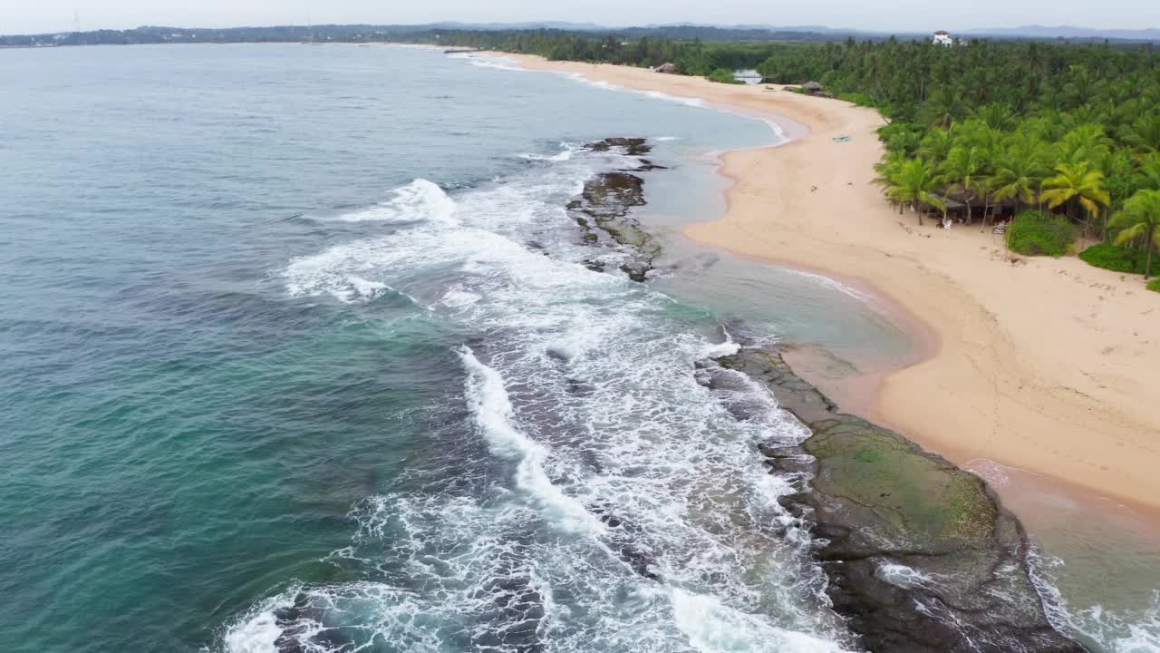 4K飞行无人机拍摄泡沫海浪在天堂岛沙滩上的岩石上翻滚。环境，异国情调的假期，生活理念。斯里兰卡的坦加勒。视频素材