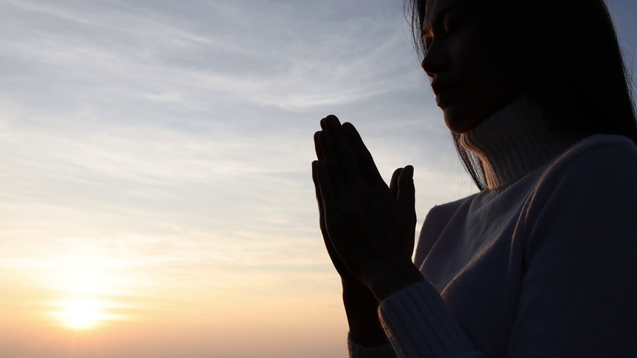 一个女人的剪影正在山上向上帝祈祷。在祝福的背景下，用对宗教的信仰和对上帝的信仰祈祷。希望、爱和奉献的力量。视频素材