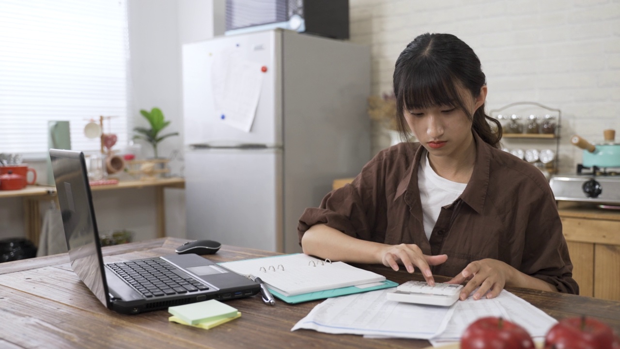 通过互联网在家工作的亚洲女会计正在现代明亮的餐厅里用计算器计算收入和预算视频素材