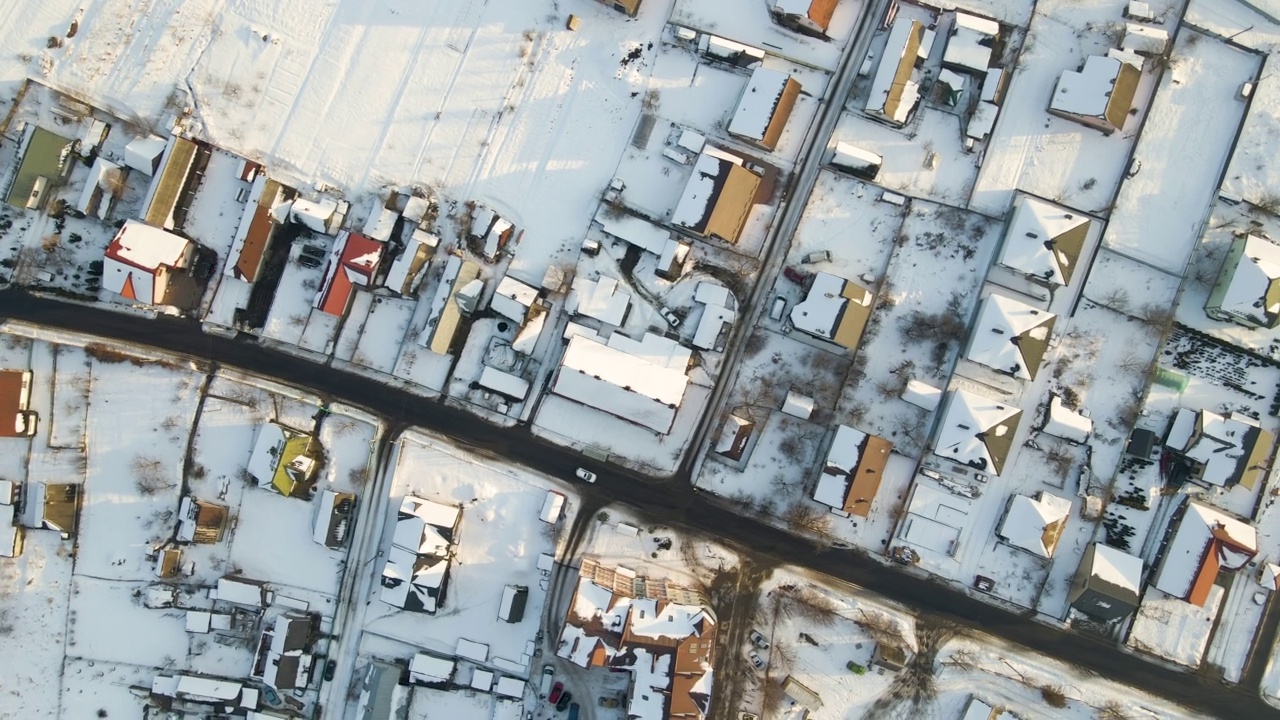 冬季城郊农村城镇地区，汽车行驶在屋顶被雪覆盖的住宅之间的街道鸟瞰图视频素材