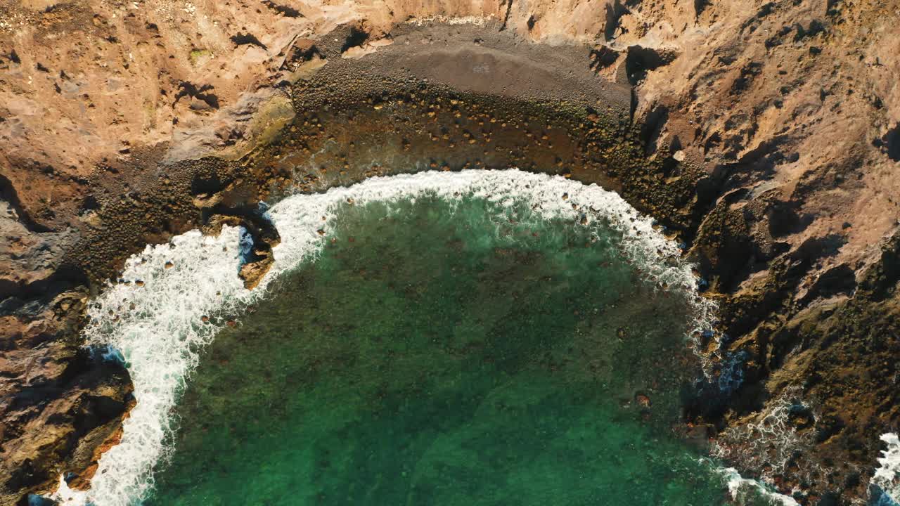 海浪拍打着空旷的热带黑色沙滩，岩石上，火山形成的岩层，石头上。狂野的海岸线遇见深蓝色碧蓝翠绿的海水。自上而下的静态鸟瞰图。视频素材