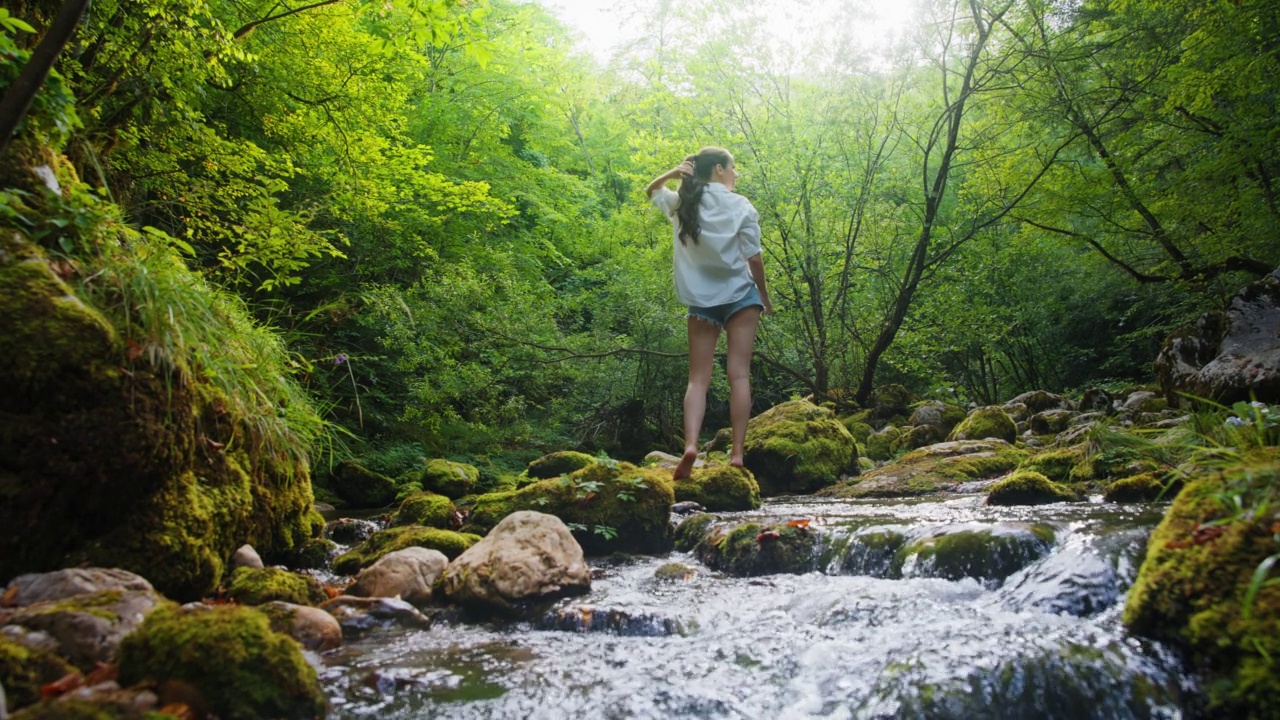 一个年轻的女人在森林里湍急的小溪边放松视频素材