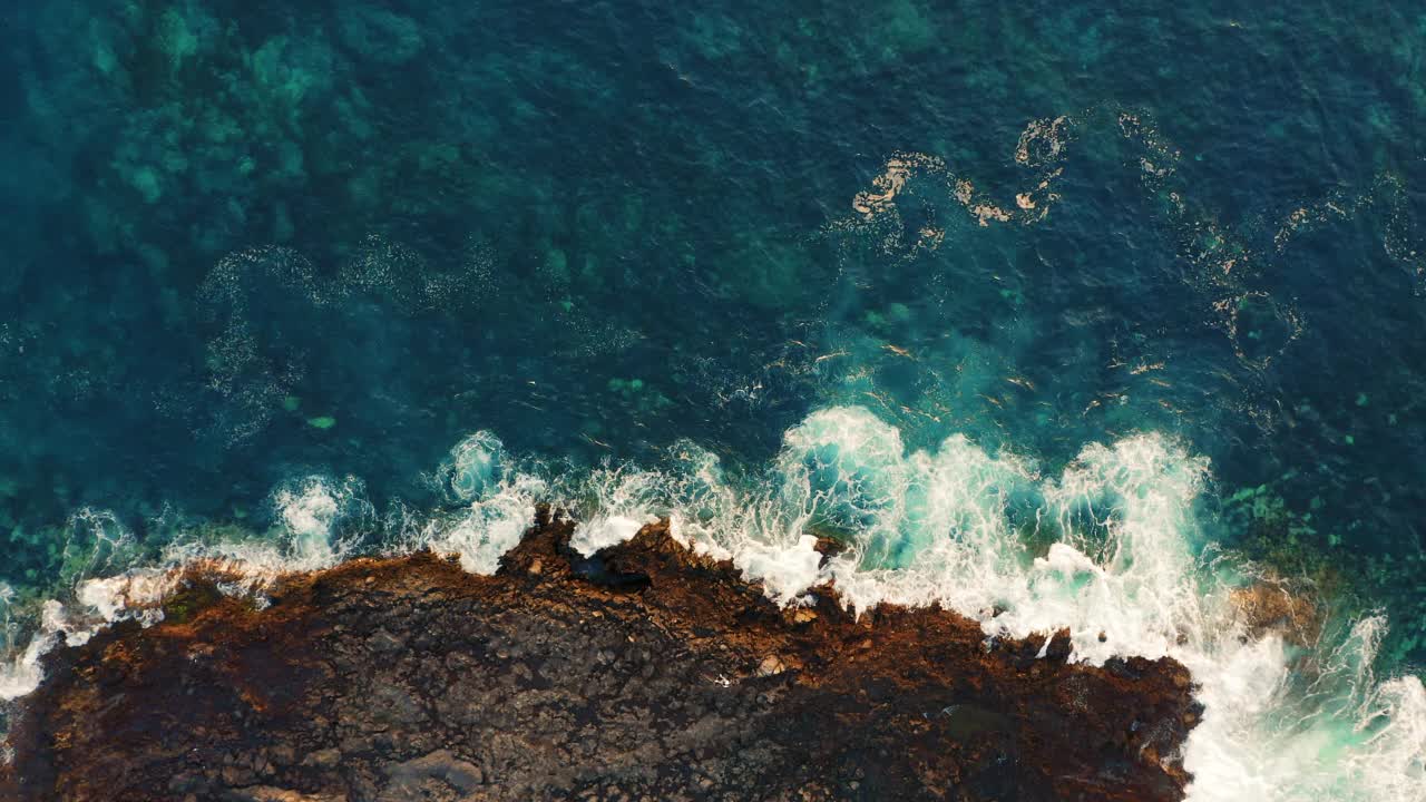 海浪在空旷的多岩石的热带海滩上拍打着泡沫，海滩上有巨大的火山构造和石头。狂野的海滩遇见深蓝色的碧水。从上面俯瞰巨大的海洋。视频素材