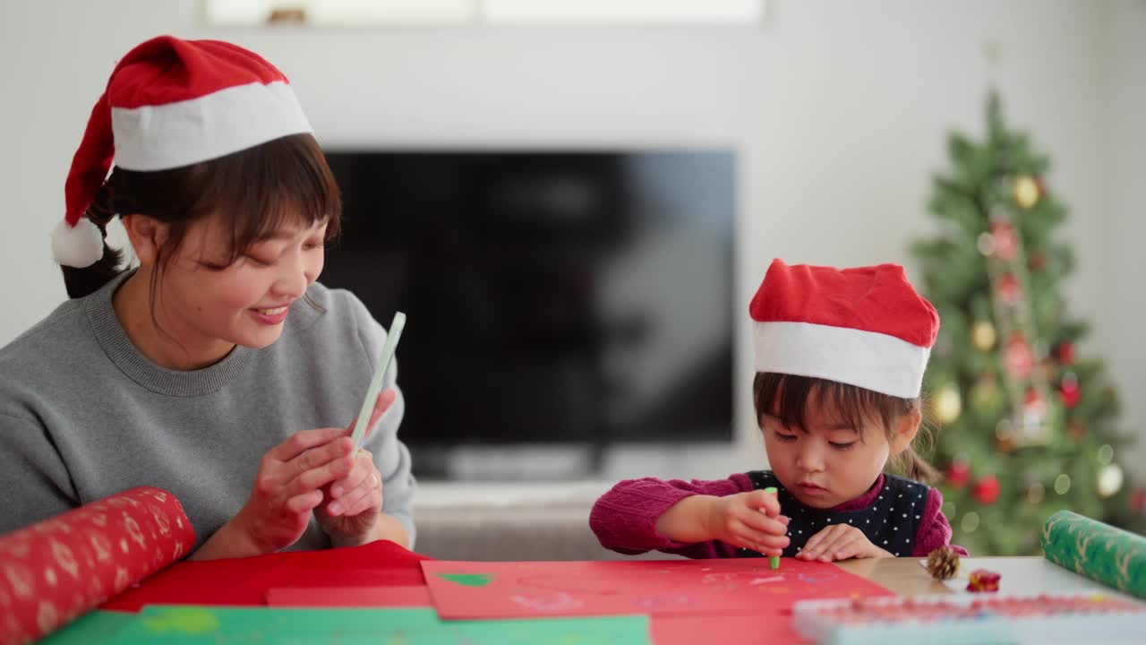 母亲正在拍摄她幼小的学龄前女儿在家里客厅diy圣诞装饰品的照片和视频视频素材