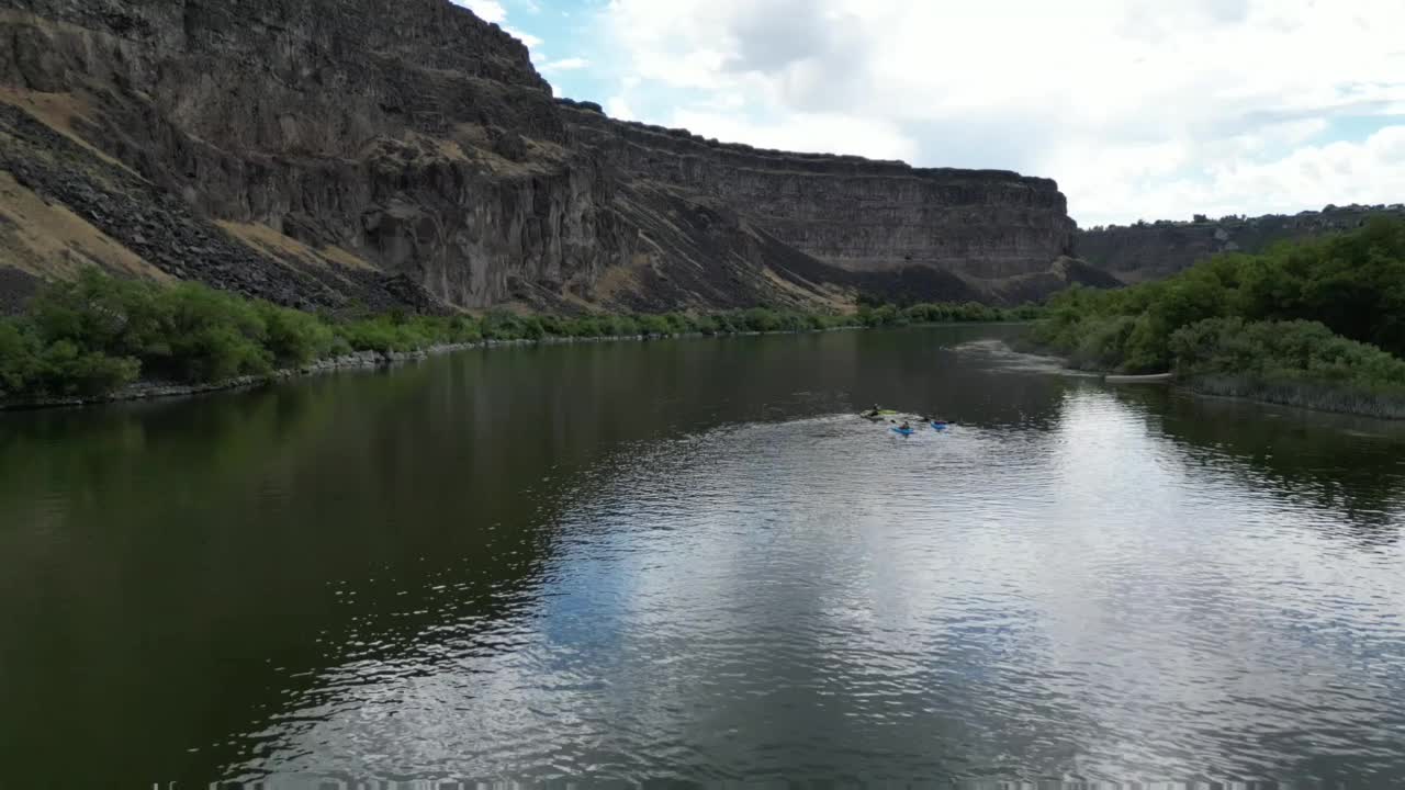 无人机在河边盘旋，河岸上有绿色植物和悬崖视频素材