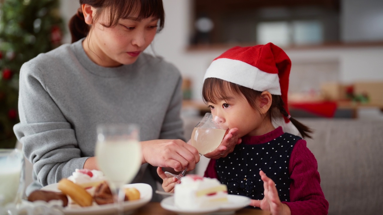 妈妈和她学龄前的小女儿坐在家里客厅的沙发上，享受着吃圣诞蛋糕和喝饮料的乐趣视频素材