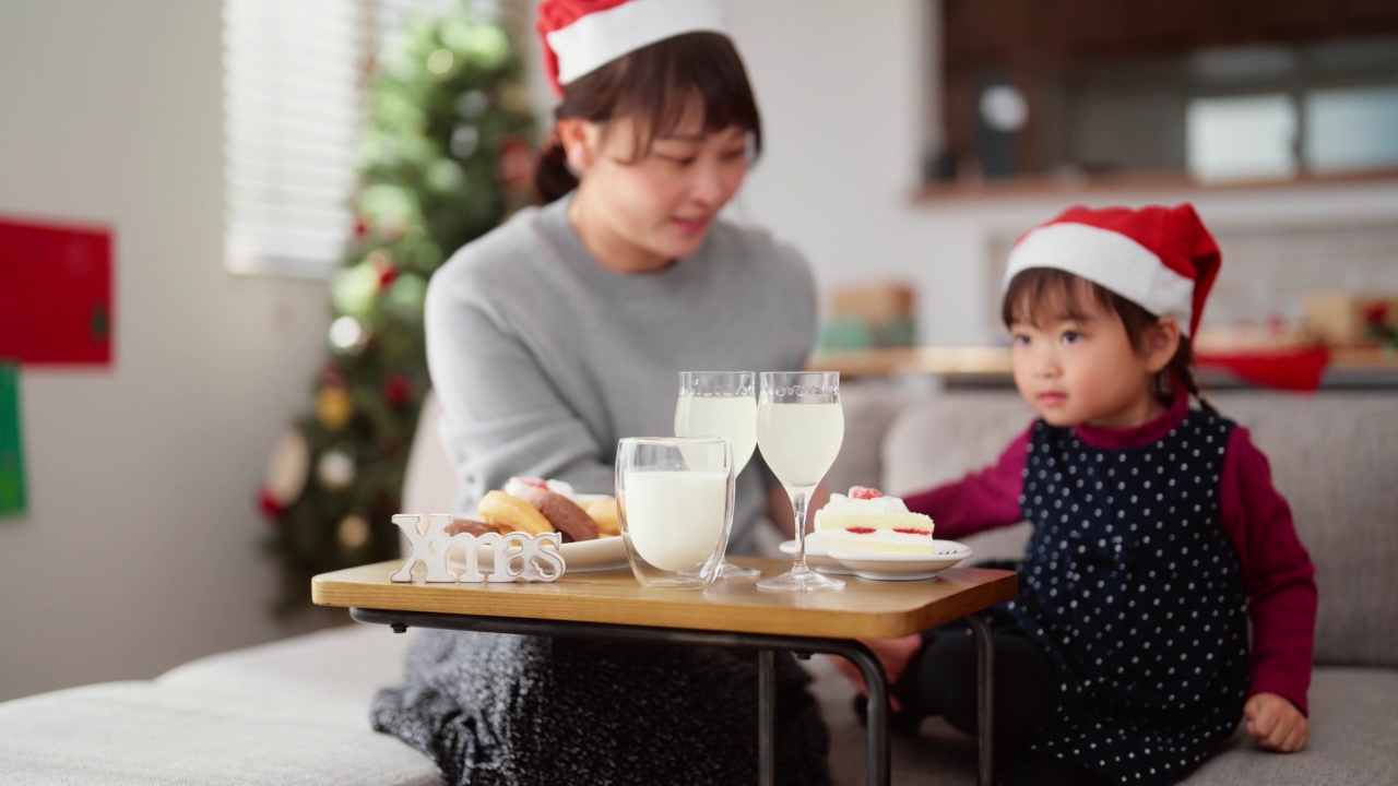 妈妈和她学龄前的小女儿坐在家里客厅的沙发上，享受着吃圣诞蛋糕和喝饮料的乐趣视频素材