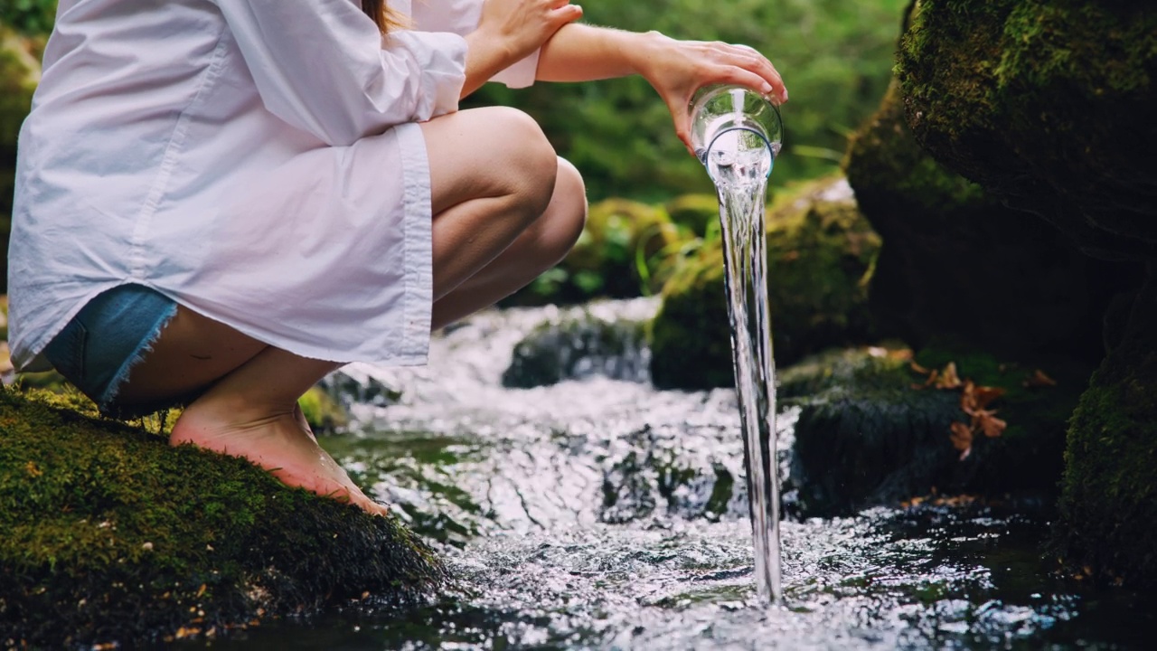 一位妇女将一壶水倒进小溪里视频素材