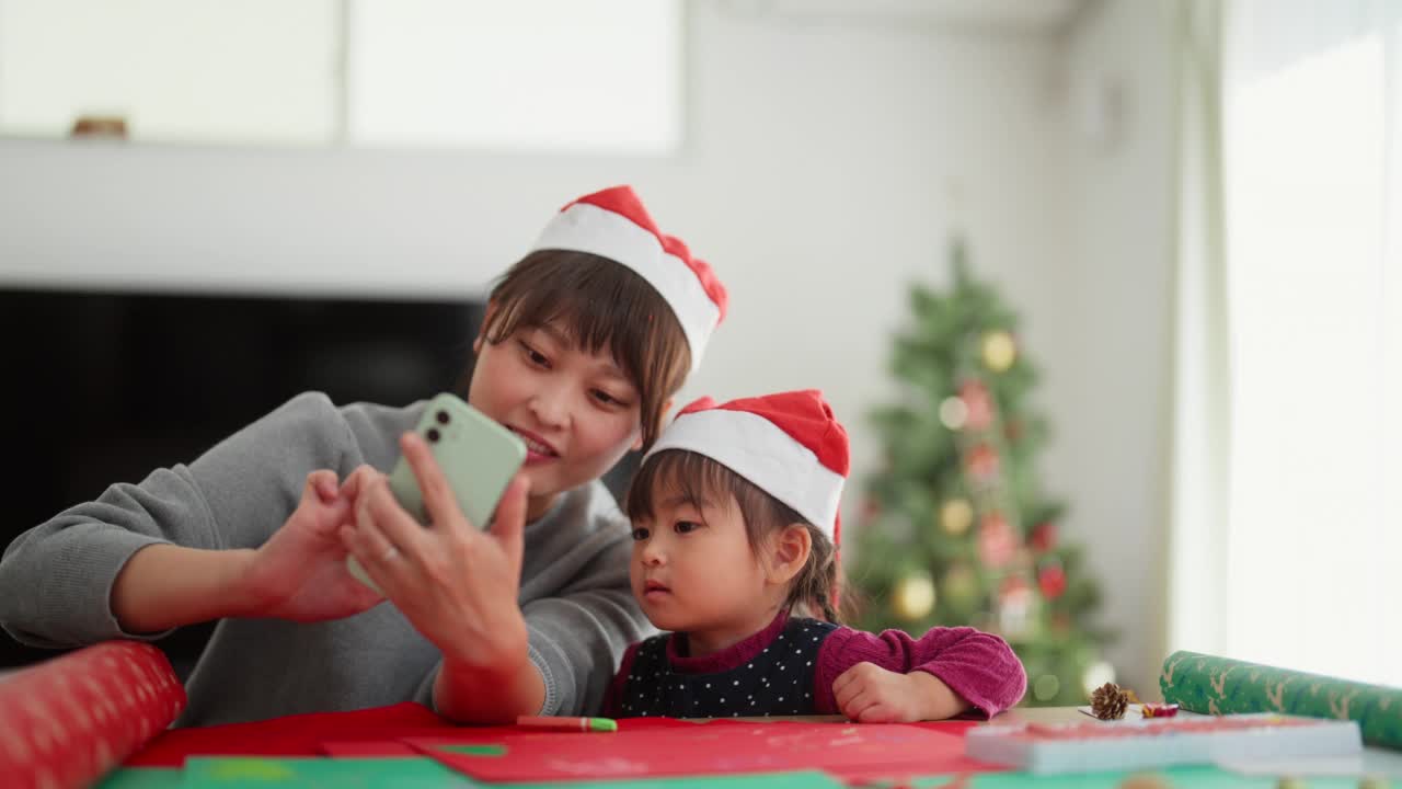 母亲和她幼小的学龄前女儿在家里的客厅里制作diy圣诞装饰，拍视频和照片视频素材