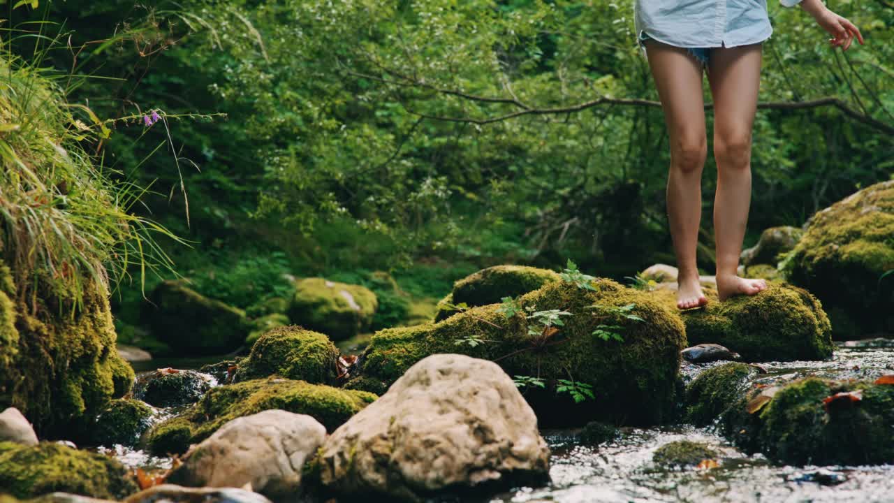 年轻女子赤脚走过小溪边的岩石视频素材