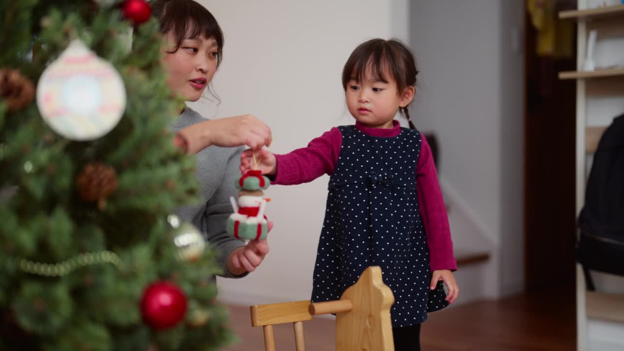 母亲和她学龄前的女儿在家里客厅装饰圣诞树视频素材