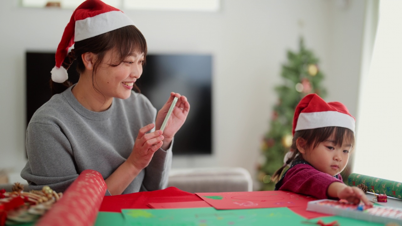 母亲正在拍摄她幼小的学龄前女儿在家里客厅diy圣诞装饰品的照片和视频视频素材