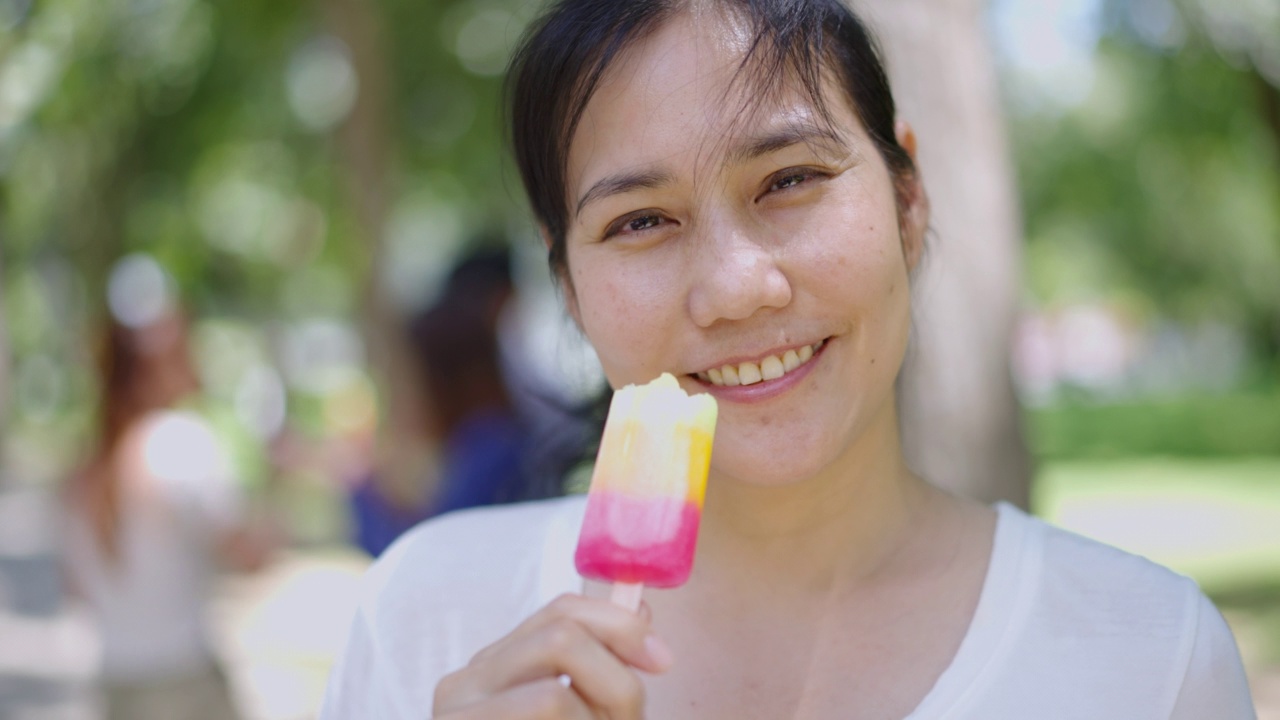 美丽的女人微笑着咬着五颜六色的冰棒冰淇淋。视频素材