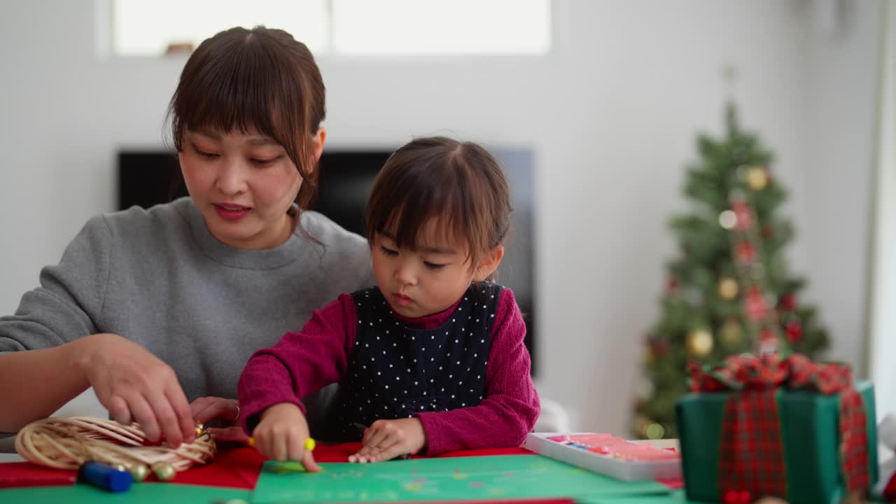 母亲和她学龄前的小女儿在家里的客厅里手工制作圣诞装饰品视频素材