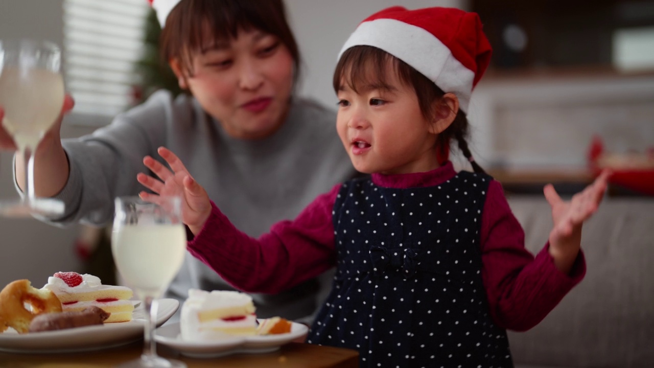 妈妈和她学龄前的小女儿坐在家里客厅的沙发上，享受着吃圣诞蛋糕和喝饮料的乐趣视频素材