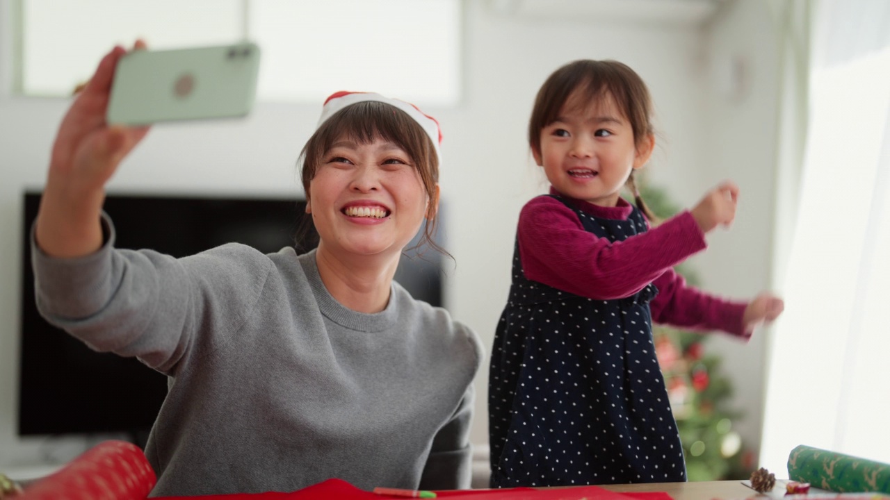 母亲和她幼小的学龄前女儿在家里的客厅里制作diy圣诞装饰，拍视频和照片视频素材