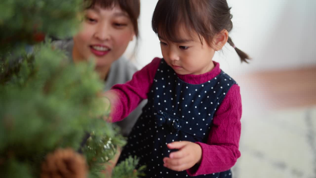 母亲和她学龄前的女儿在家里客厅装饰圣诞树视频素材