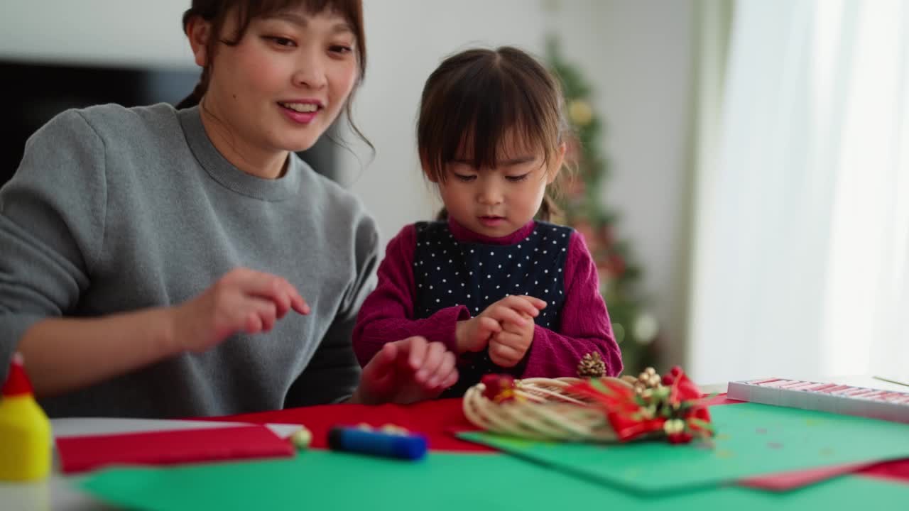 母亲和她学龄前的小女儿在家里的客厅里手工制作圣诞装饰品视频素材