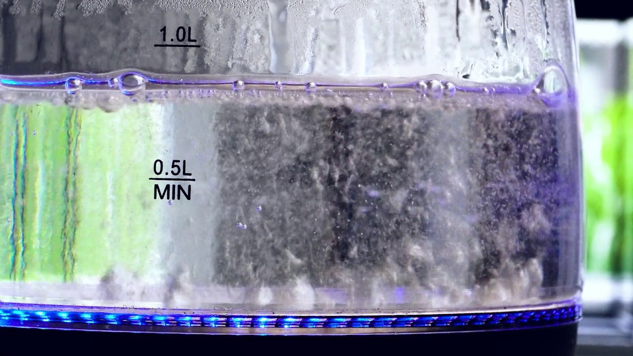 透明电热水壶，里面有沸腾的水，厨房桌子上有蓝色的霓虹灯背光视频素材