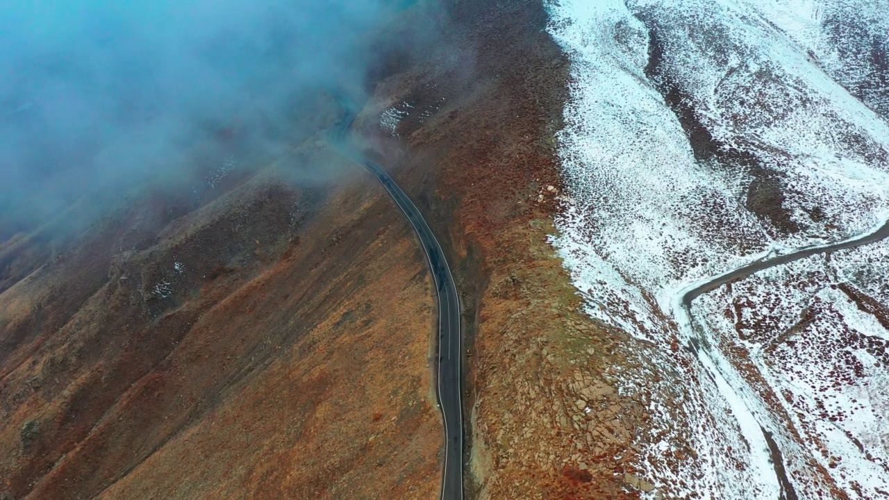 在无人机跟踪下，在山峰上穿越雾和雪的公路旅行视频素材