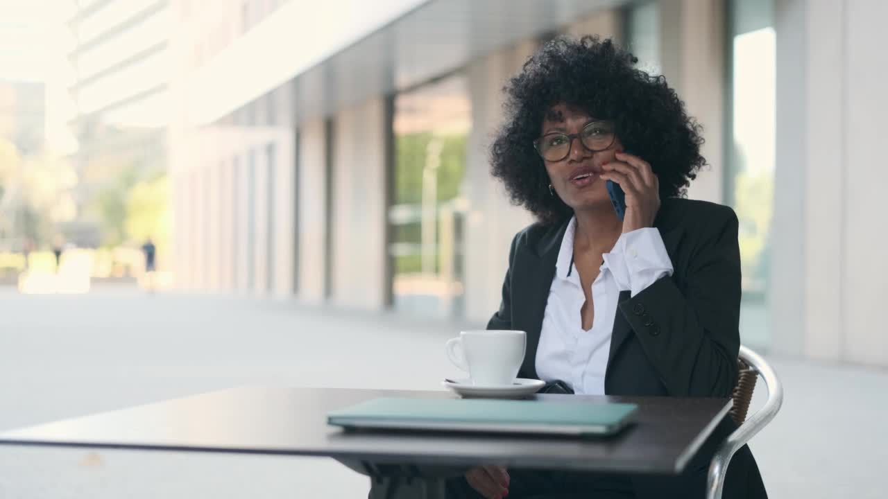 一位女商人坐在金融区的一家户外咖啡馆里打电话。视频素材