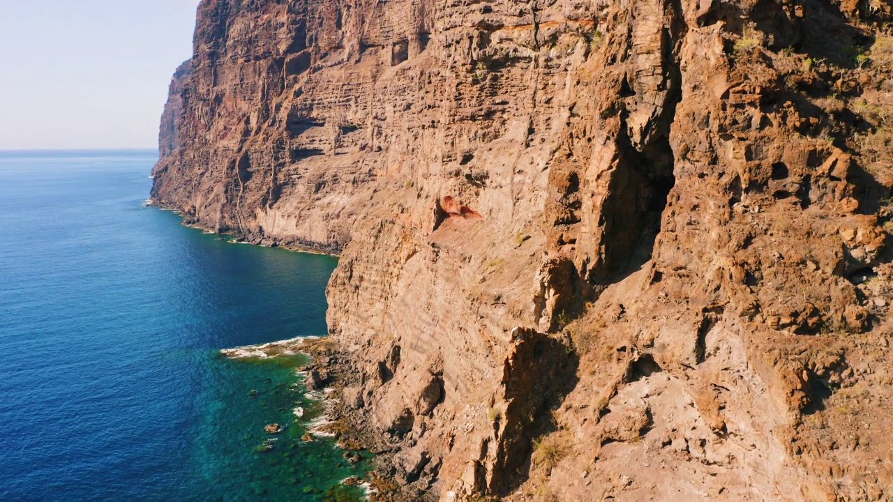 空中倾斜拍摄到海洋中岩石嶙峋的空悬崖。大西洋海岸。美丽的大自然，特内里费岛。暑假旅游的概念。巨大的岩石贫瘠的山脉。深蓝色透明的水。视频素材