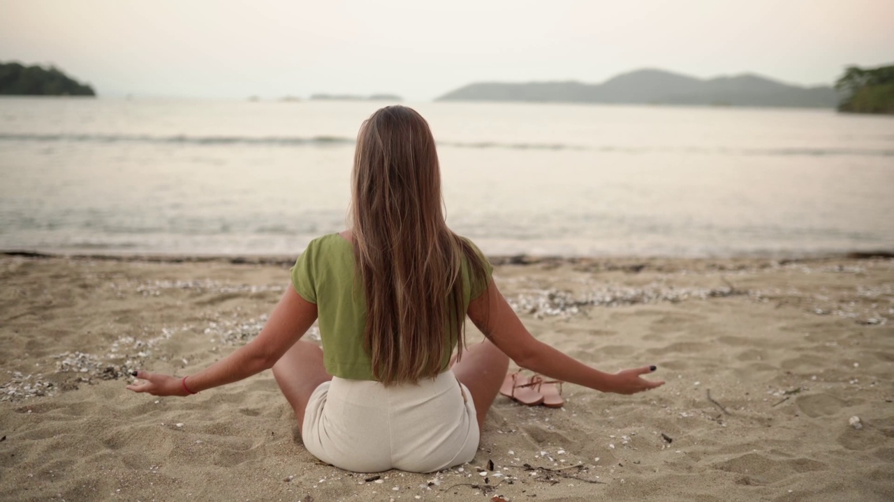 女人在夕阳下的海滩上冥想视频素材