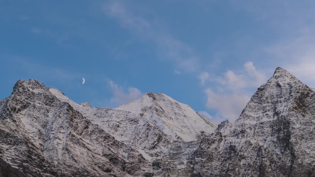 在印度喜马偕尔邦拉胡尔，月亮在积雪覆盖的喜马拉雅山脉的多云天空中移动的4K时间间隔。冬天，在雪山上，傍晚日落的天空渐渐消逝。视频素材