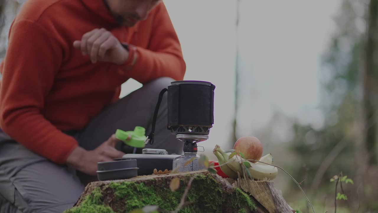 徒步旅行者准备食物，从瓶子里把水倒进锅里。森林里的旅行者用小炉灶做饭。背包客使用烹饪系统。男往煤气炉筒里注水。视频素材