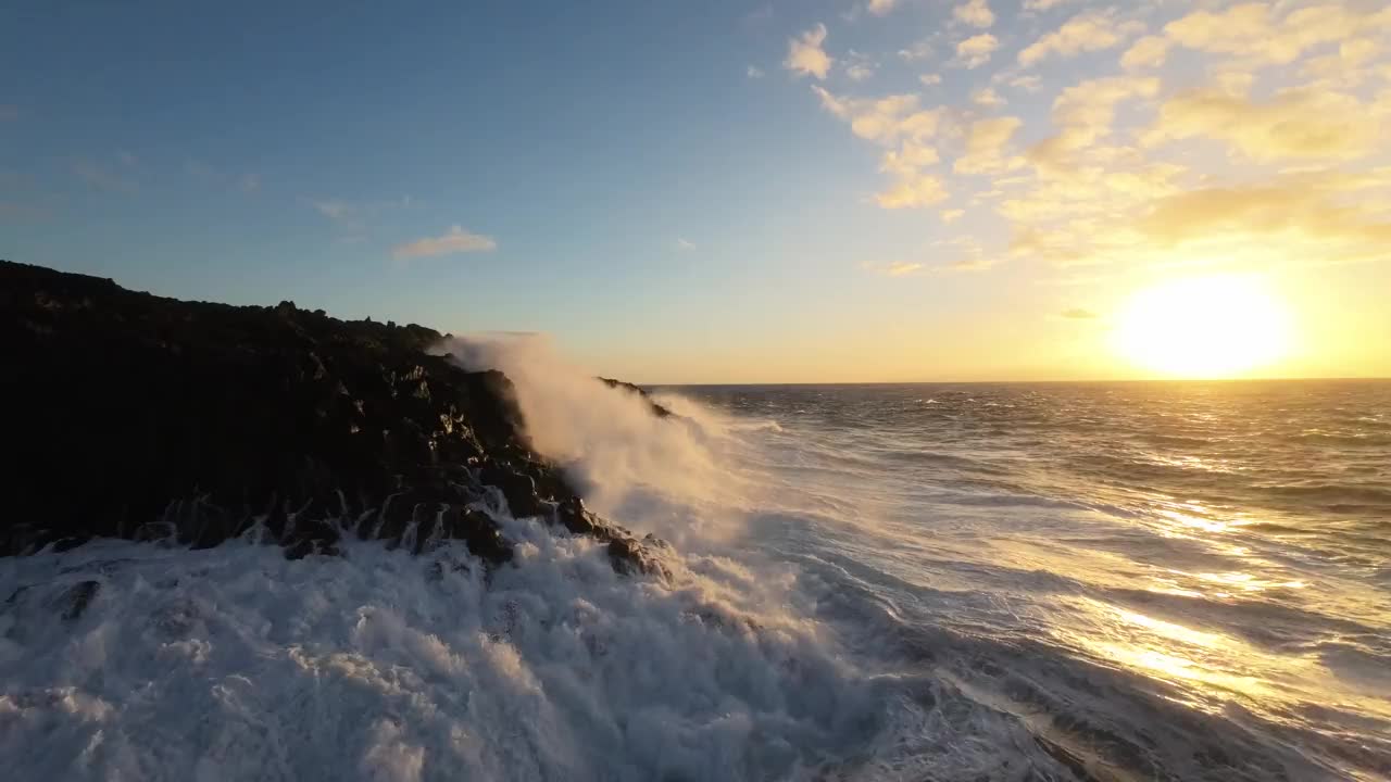 航拍飞行非常近的泡沫浪花海洋撞击岩石海岸由日落岩石视频素材