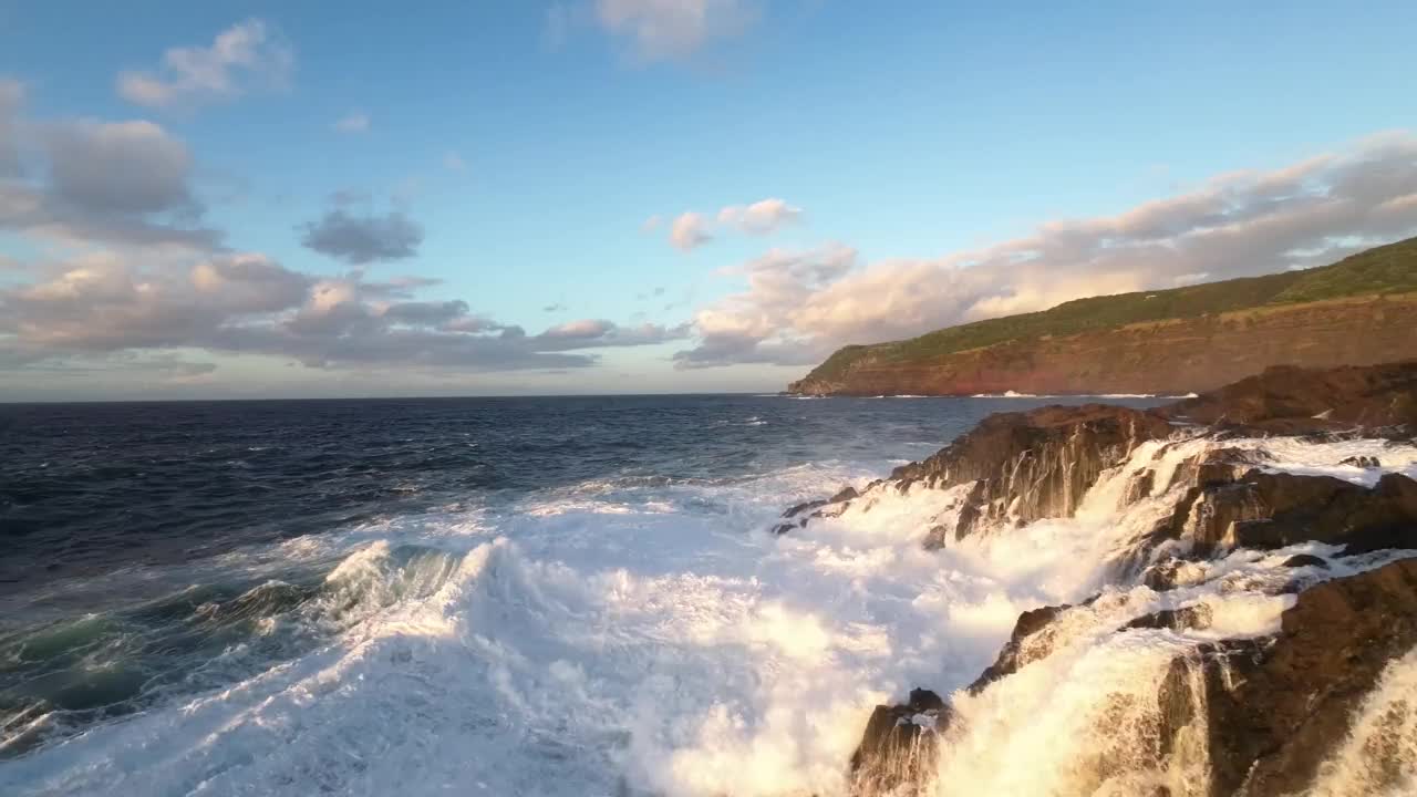 航拍飞行非常近的泡沫浪花海洋撞击岩石海岸由日落岩石视频素材