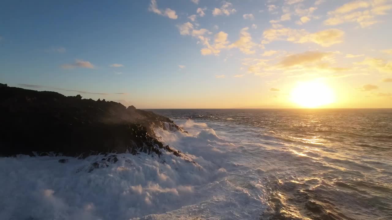 航拍飞行非常近的泡沫浪花海洋撞击岩石海岸由日落岩石视频素材