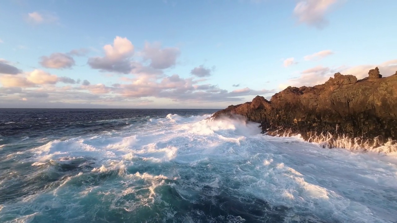 航拍飞行非常近的泡沫浪花海洋撞击岩石海岸由日落岩石视频素材