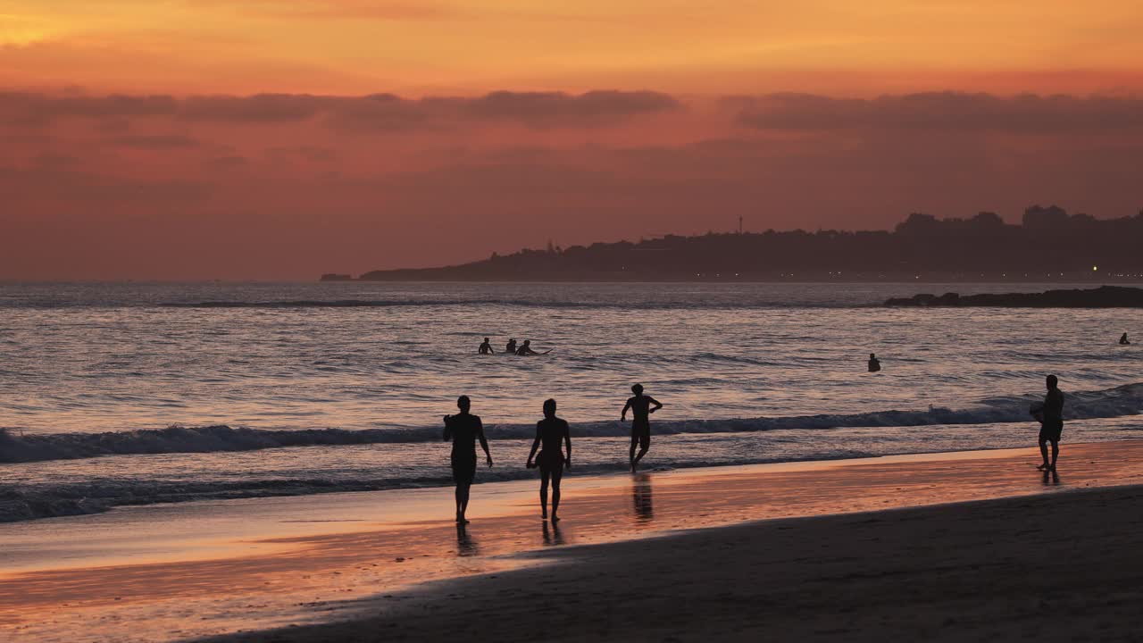 人们走在沙滩上的剪影和冲浪者在夕阳背景下的大西洋海岸葡萄牙。视频素材